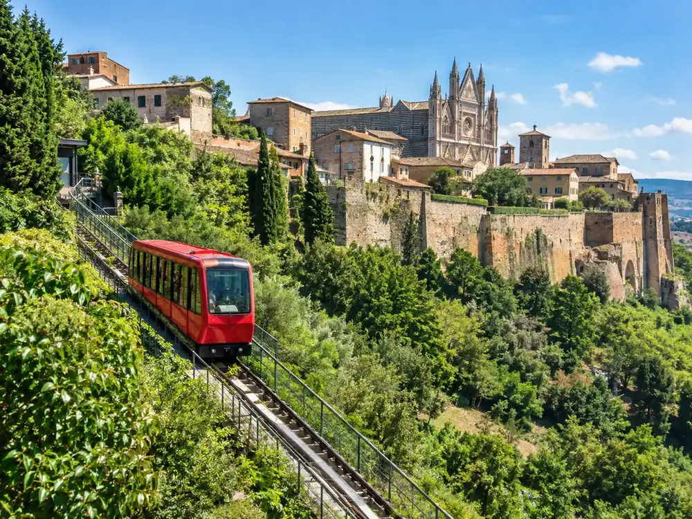 A red funicular car climbing the green hillside below the walls of Orvieto